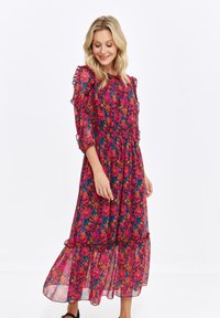 Floral midi dress in sheer fabric, featuring red, pink, and blue flowers, ruffled sleeves, and a tiered skirt with a flowy silhouette.