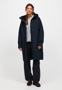 Giacca impermeabile blu navy con cappuccio, bottoni a pressione e chiusura con zip. Caratterizzata da una vestibilità ampia, tasche e polsini regolabili per la protezione dalle intemperie.
