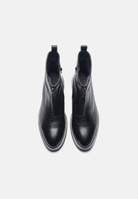 Botas de tobillo de cuero negro con cremallera lateral, punta redonda y textura suave. Mostradas desde arriba, mostrando el diseño y la costura.