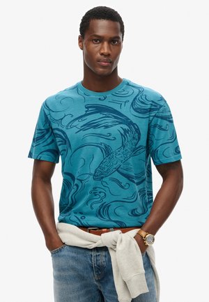 Camiseta de algodón en color verde azulado con un patrón de peces y olas en tonos más oscuros, con un clásico escote redondo y mangas cortas.