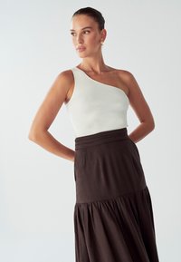 Biela rebrovaná top na jedno rameno v kombinácii s dlhou, tmavohnedou sukňou s viacerými vrstvami. Sukňa má priliehavý pás a voľnejšiu dolnú časť.