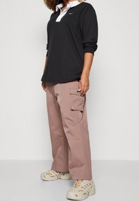 Černý tričko s dlouhým rukávem a bílým límečkem, doplněné volnými růžovými cargo kalhotami se bočními kapsami a krémovými botami.