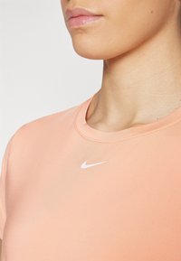 Camiseta ajustada de manga corta de Nike en color melocotón claro con una textura suave y un logo Swoosh blanco en el pecho. Cuello redondo.