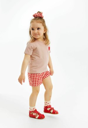 T-shirt rosa chiaro con un toppe a forma di cuore rossa, pantaloni corto a quadretti rossi e bianchi, sandali rossi e calzini a motivi a cuore. Scrunchie nei capelli.