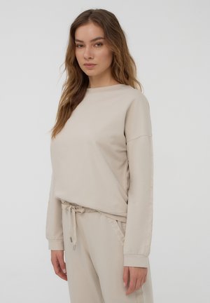 Felpa beige con maniche lunghe, scollo rotondo e vestibilità rilassata. Presenta dettagli laterali testurizzati e polsini elasticizzati; tessuto morbido.