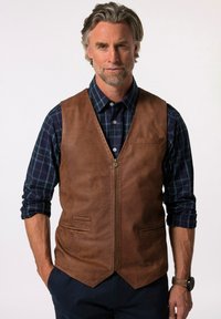 Chaleco de cuero marrón con cierre de cremallera, dos bolsillos frontales y diseño de escote en V, llevado sobre una camisa de cuadros azul. Textura suave y líneas limpias.