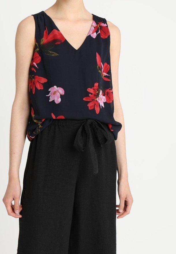Haut sans manches bleu marine avec imprimé floral rouge et rose, associé à un pantalon noir à jambes larges noué à la taille avec une ceinture en tissu.
