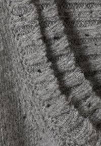 Gros plan sur un tissu tricoté gris texturé avec des fibres douces et duveteuses, et des points côtelés et décoratifs créant une apparence chaleureuse.