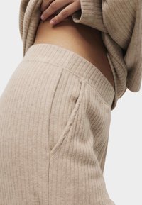 Béžové žebrované kalhoty na doma s přiléhavým pasem, bočními kapsami a měkkou texturou, zdůrazňující jemné liniové vzory po celé ploše.