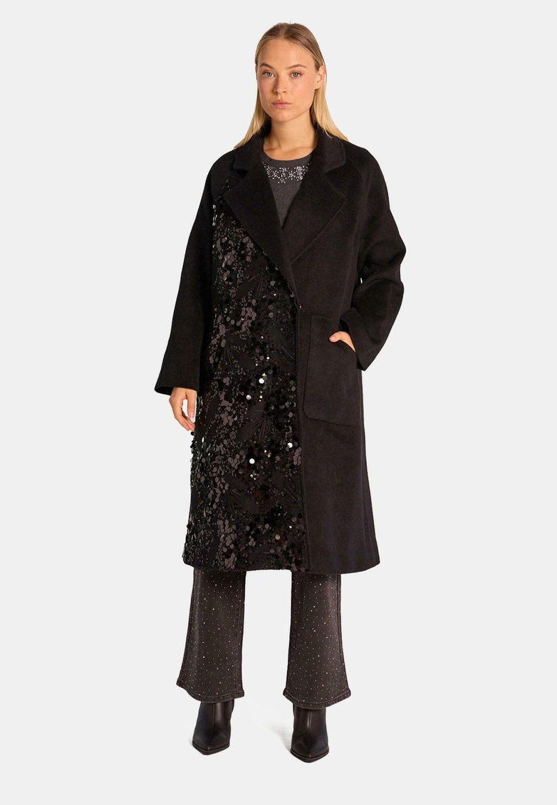 Cappotto nero con un tessuto texturizzato caratterizzato da un design floreale in paillettes su un lato. Ha un colletto, vestibilità regolare e tasche laterali.