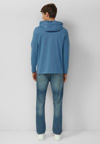 Niebieska bluza z kapturem z długimi rękawami, zestawiona z wyblakłymi niebieskimi dżinsami. Materiał wydaje się miękki, z casualowym wzorem i luźnym krojem.