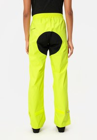 Vaudé waterproof pants in bright neon yellow, featuring a black circular accent on the back, elastic waistband, and Velcro cuffs.