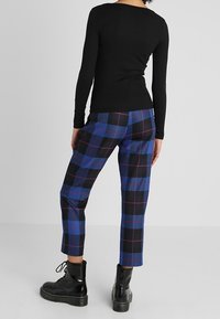 Haut à manches longues noir associé à un pantalon cropped à carreaux bleus avec des accents noirs et rouges, complété par des bottes à lacets brillantes noires.