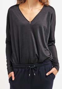 Black long-sleeve top with a V-neck and a subtle front seam. Soft, lightweight fabric with a relaxed fit, paired with navy drawstring pants.