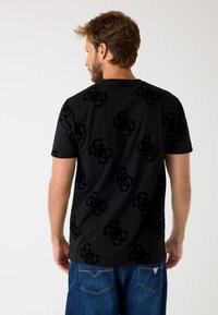 Sort t-shirt med et tekstureret sort logo mønster. Rund hals og korte ærmer, parret med blå denim jeans. Afslappet pasform.