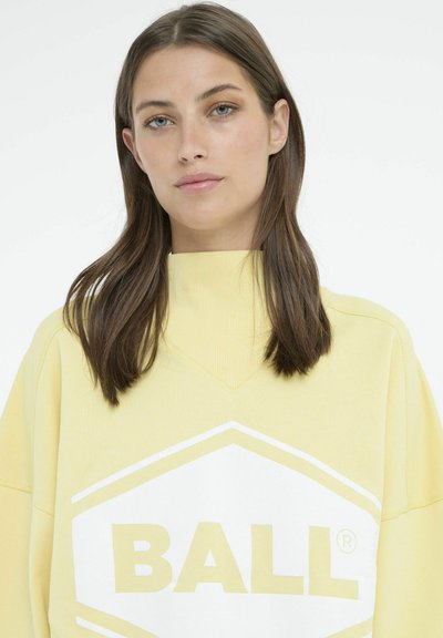 Gul sweatshirt lavet af blødt stof, med et hvidt sekskantet logo, der har "BALL" i fede bogstaver. Høj krave og afslappet pasform.