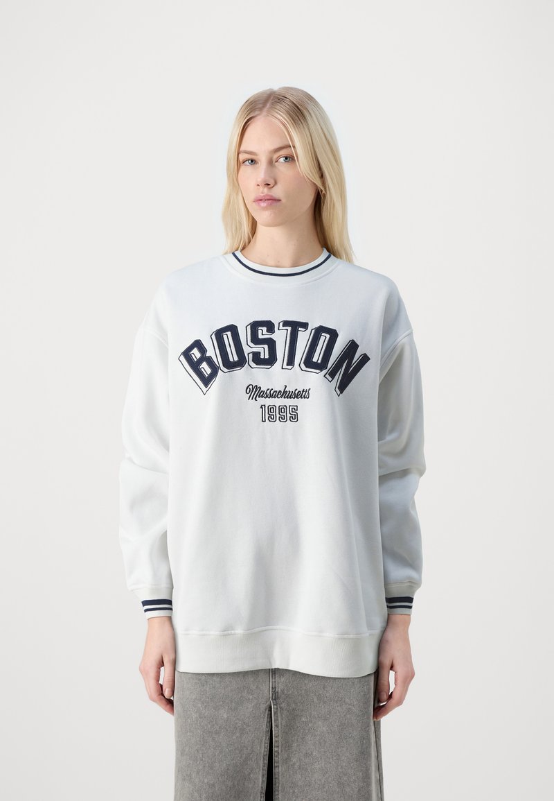 Sudadera blanca con "BOSTON" y "Massachusetts 1995" en color marino, cuello de crew acanalado y acentos a rayas en los puños y el dobladillo. Corte relajado.