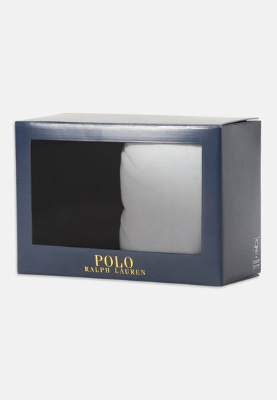 Dėžė su skaidriu priekiu, kurioje matomas baltas produktas. Tamsiai mėlyna išorė su auksiniu "POLO RALPH LAUREN" užrašu apačioje.