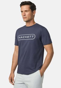 Námořnicky modré bavlněné tričko s kulatým výstřihem, s bílým logem "HACKETT" v oválném tvaru na hrudi. Hladká textura.