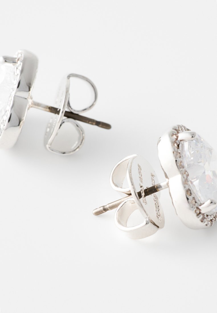 Srebrne kolczyki na stud, z przezroczystym, fasetowanym kamieniem otoczonym teksturowanym brzegiem. Projekt zawiera zapięcie motylkowe dla zapewnienia bezpieczeństwa noszenia.