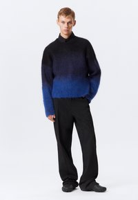 Maglione a maglia blu e nero con un colletto alto, abbinato a pantaloni neri a righe e scarpe nere texture.