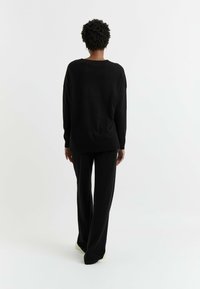 Maglione nero a maglia con vestibilità ampia e spalle cadenti, abbinato a pantaloni neri larghi coordinati, visto da dietro.