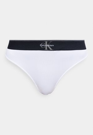 Balti kokvilnas biksītes ar melnu elastīgu jostu, kurā ir Calvin Klein logotips pelēkā un baltā krāsā.
