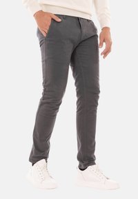 Pantaloni slim-fit grigi in cotone con una texture liscia, dotati di tasche frontali e un design frontale piatto. Indossati con sneaker bianche.