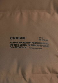 Tela marrón con texto en negrita negro: "CHASIN', EST. 92, FUENTE REAL DE RENDIMIENTO, VISIÓN INFINITA EN FORMAS INFINITAS, www.chasin.com."