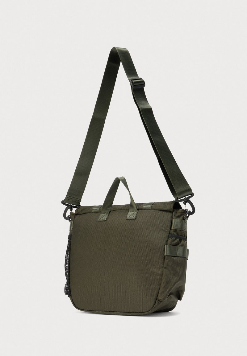 Sac à bandoulière vert foncé avec sangle réglable, poignées supérieures, poches latérales et porte-bouteille en filet, sur un fond uni.