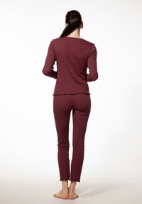 Bordeaux tweedelig pyjama-set met lange mouwen en aansluitende broek. Rimpelige randjes op het bovenstuk en de broek, gemaakt van zachte, rekbare stof.
