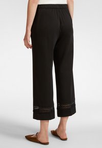 Pantaloni neri a gamba larga realizzati in tessuto morbido, con dettagli in pizzo all'orlo e una vita elasticizzata per il massimo comfort.