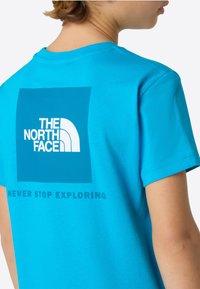 Turquoise cotton t-shirt featuring a white rectangle with "THE NORTH FACE" logo and "NEVER STOP EXPLORING" text in bold, modern font.