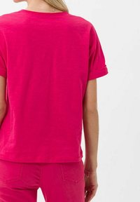 Tílko s krátkým rukávem a kulatým výstřihem v jasně růžové barvě, se zulámanými rukávy a volným střihem, vyrobené z lehkého materiálu.