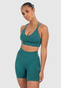 Conjunto de sujetador deportivo en color teal y pantalones cortos de cintura alta. Sujetador con escote en V y centro fruncido; los pantalones cortos presentan un acabado suave y acentos texturizados.