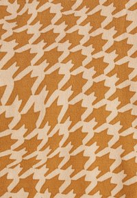 Tessuto texturizzato con un motivo a scacchi in tonalità marrone dorato e beige, caratterizzato da forme a zigzag distinte in tutto il design.