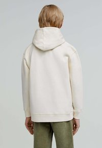 Felpa con cappuccio crema dal taglio rilassato, morbido al tatto, con polsini a costine, abbinata a pantaloni verdi con texture.