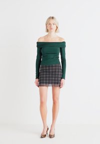 Grønn off-shoulder topp med lange ermer, kombinert med en gjennomsiktig rutete mini skjørt, med mykt stoff og en tettsittende design. Akkompagnert av høyhælte sko med dyreprint.