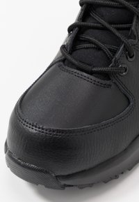 Scarpa atletica nera con punta in pelle testurizzata, tomaia liscia in materiale sintetico e suola robusta in gomma con dettagli scolpiti.