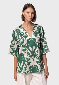 Blusa ampia in tessuto crema con audace motivo floreale verde, scollatura a V e maniche a tre quarti. Texture liscia e design rilassato.