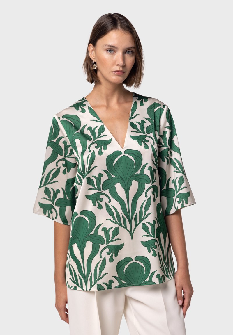 Blusa ampia in tessuto crema con audace motivo floreale verde, scollatura a V e maniche a tre quarti. Texture liscia e design rilassato.