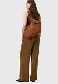 Borsa a tracolla in suede marrone, morbida e con una patta piegata, caratterizzata da accenti scuri e una tracolla testurizzata.