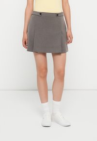 Szara plisowana mini spódniczka z dwoma czarnymi guzikami w talii. Materiał wydaje się gładki, uzupełniony prostym, klasycznym krojem.