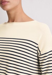 Gestreepte trui in crème en marineblauw, met een boothals en zachte, gestructureerde stof; horizontale strepen bedekken het bovenlichaam.