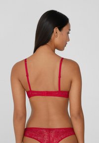 Červená krajková podprsenka a odpovídající kalhotky, s tenkými ramínky, květinovými vzory, jemnou strukturou a háčkovým zapínáním na zadní straně.