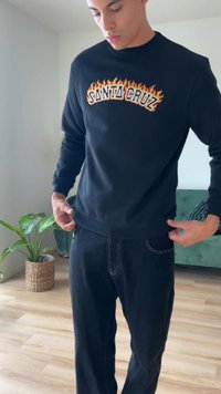 Sweatshirt preto com a inscrição "SANTA CRUZ" em letras laranja e amarelo ardente. Combinado com calças escuras, exibindo detalhes de costura contrastantes.