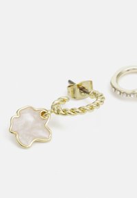 Gold hoop earring with a twisted design, featuring a translucent flower-shaped detail in a pale color. Includes a post backing.