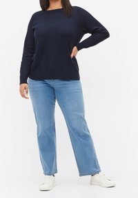 Marinblå tröja med fiskbensmönster, rund halsringning och ribbade muddar, ihop med ljusblå vida jeans och vita sneakers.