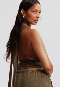 Top olive vert sans dos avec des bretelles à nouer, associé à un pantalon à taille élastique assortie. Texture lisse, design minimal, avec un dos plongeant.