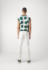 Sleeveless white sweater with green polka dots, paired with white jeans and black sneakers featuring green accents. Visible stitching details.